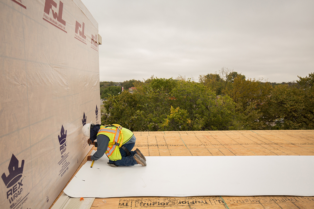 A worker measures and cuts on the rooftops of townhomes built by a joint effort between Eko and Durham Builders. (Photo by Rasy Ran)