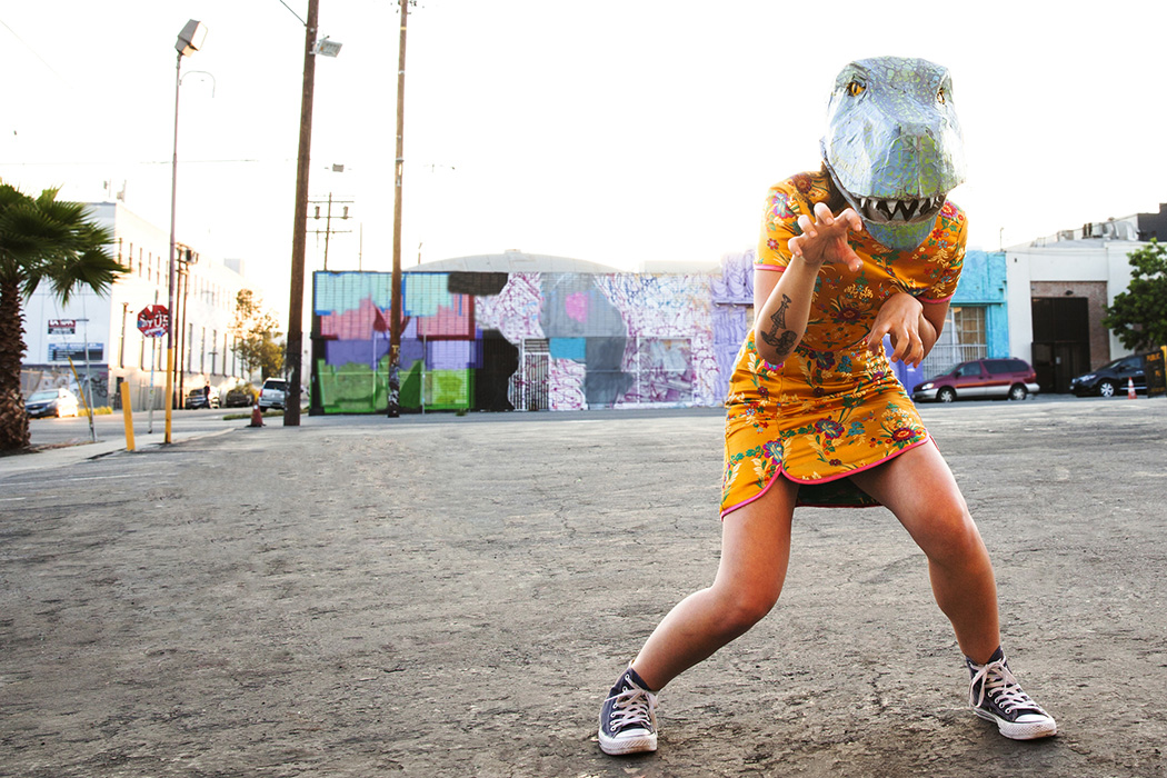 Young woman wearing a handmade dinosaur mask in an empty parking lot