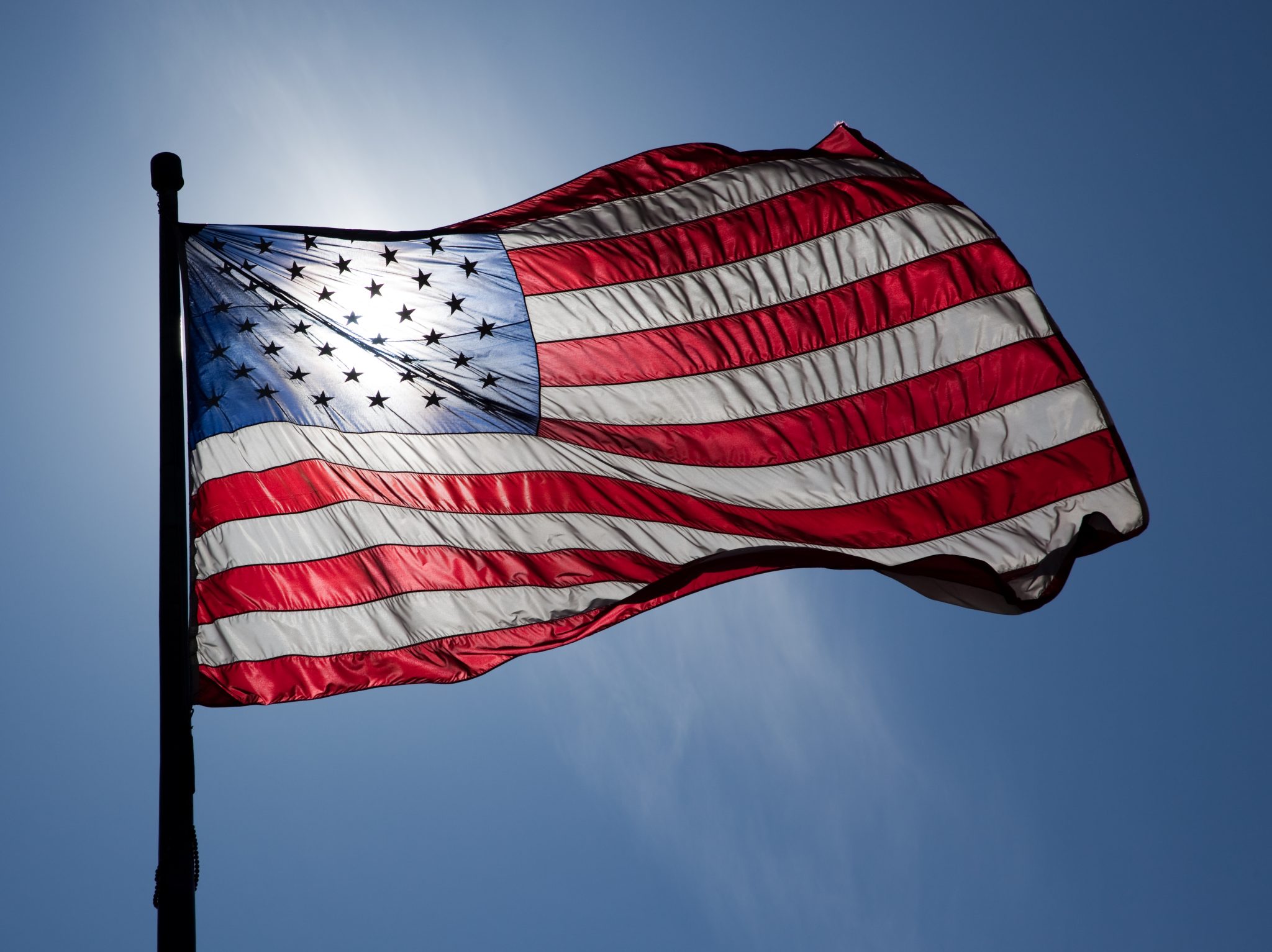 An American flag. The sun is behind it, shining through the stars on the flag.