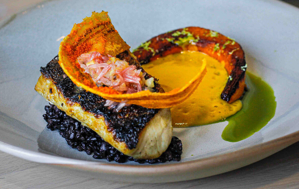 The grilled sea bass sits on a bed of forbidden (black) rice, pumpkin coconut velouté and pomelo chutney. Photography by Kelsey Shoemaker