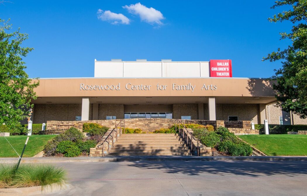 A building with a concrete awning. It says "Rosewood Center for the Family Arts" and above that, "Dallas Children's Theater." The property is landscaped with grass, shrubs and trees.