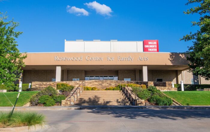 A building with a concrete awning. It says "Rosewood Center for the Family Arts" and above that, "Dallas Children's Theater." The property is landscaped with grass, shrubs and trees.